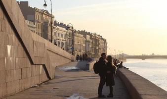 Sankt Petersburgo Rusia - 04 10 2023 dos amantes besos a puesta de sol en río costa. contento calle Moda estilo Pareja abarcar. encantador joven hombre y mujer abrazando en ajuste luz de sol. foto