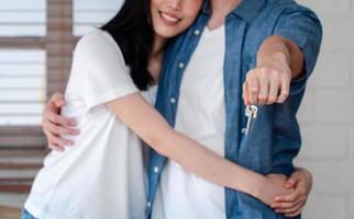 Happy smiling couple in front of the home and holding keys to New Home On Moving In Day, and start a new life family. Concept of homeowner and relocation photo