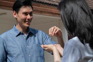 Happy smiling couple in front of the home and holding keys to New Home On Moving In Day, and start a new life family. Concept of homeowner and relocation photo