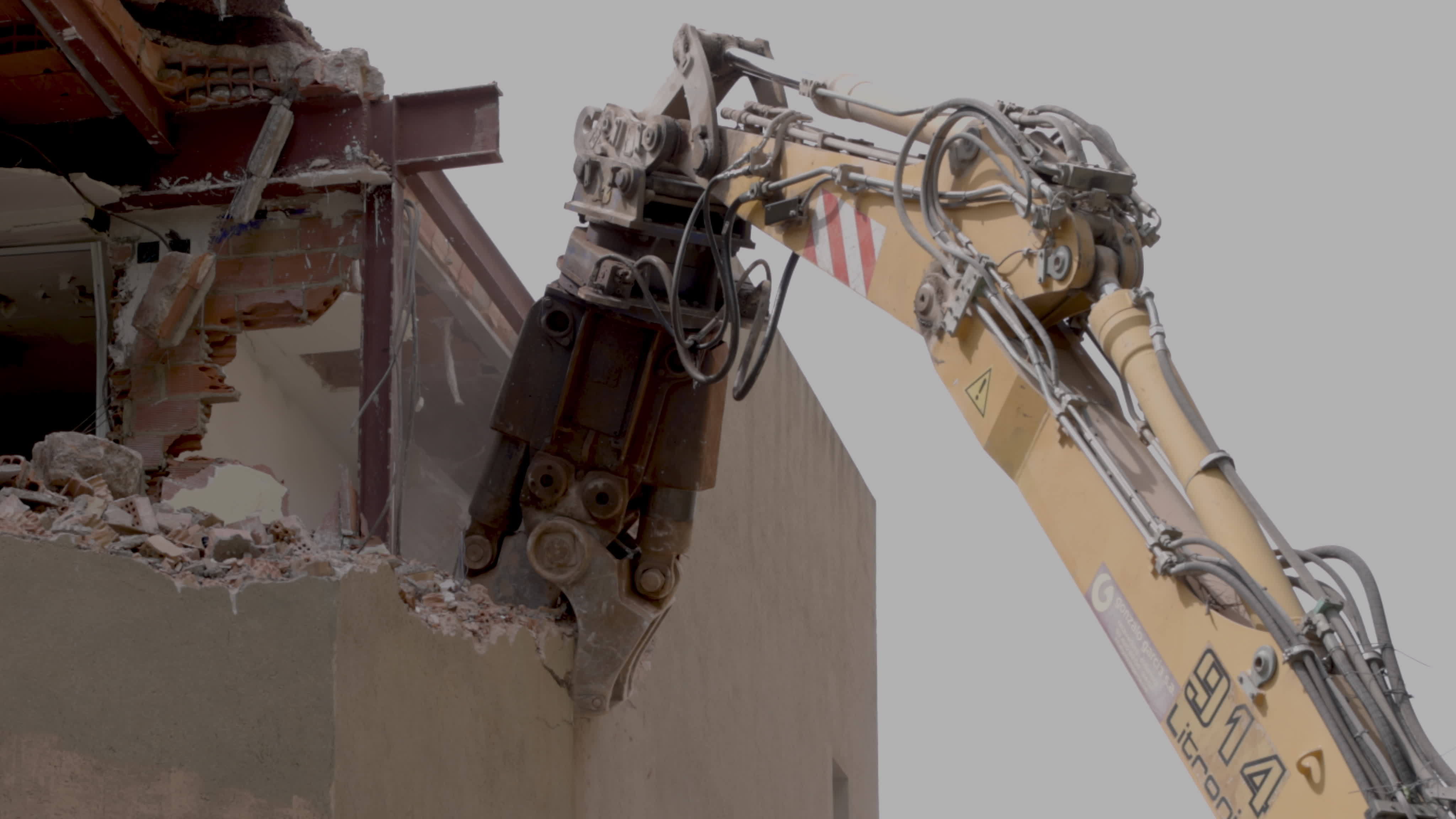 mechanical jaws on the end of a crane tear down an old building in slow