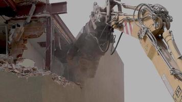 mechanical jaws on the end of a crane tear down an old building in slow motion video