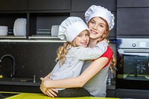 Two girls with chef hat hugging and having fun in kitchen photo