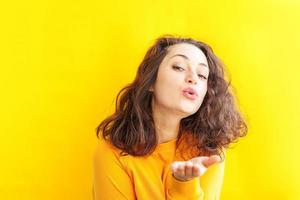 Love, peace. Beauty portrait young happy positive woman posing with kiss face expression showing love sign on yellow background isolated. European girl. Positive human emotion. photo