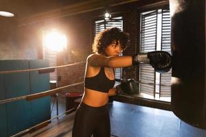 mujer yo defensa niña fuerza. africano americano mujer combatiente formación puñetazos en boxeo anillo. sano fuerte niña puñetazos boxeo bolsa. formación día en boxeo gimnasia. fuerza ajuste cuerpo rutina de ejercicio capacitación. foto