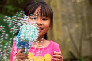 A little girl uses a play gun to blow soap bubbles in a summer park. Background toning for the Instagram filter. photo