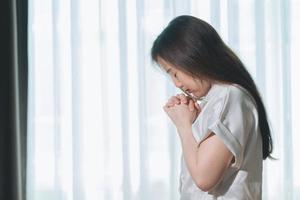 Hopeful make wish, calm asian young woman belief, hand in prayer, sitting meditating on sofa at home, Christian girl praying to God for ask, request with closed eyes dreaming for help, thanks you God. photo