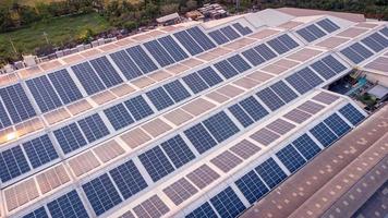 un grande solar célula techo en un industrial edificio generando electricidad para el planta durante tiempo de día según a políticas y medidas a reducir global calentamiento por tomando Angulo alto disparos desde drones foto