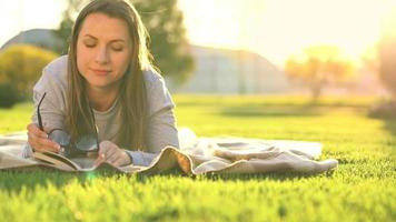 Mädchen im Brille lesen Buch Lügen Nieder auf ein Decke im das Park beim Sonnenuntergang video