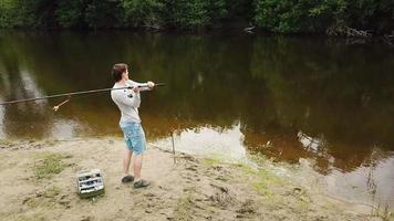 pescador con un pescar varilla en el río banco. hombre pescador capturas un pescado video