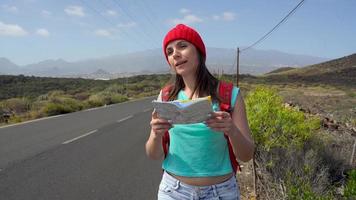 Traveler woman hitchhiking on a sunny road and walking. Backpacker woman looking for a ride to start a journey on a sunlit country road. Slow motion video