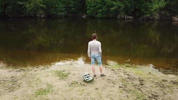 Fischer mit ein Angeln Stange auf das Fluss Bank. Mann Fischer fängt ein Fisch video