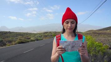 Traveler woman hitchhiking on a sunny road and walking. Backpacker woman looking for a ride to start a journey on a sunlit country road. Slow motion video