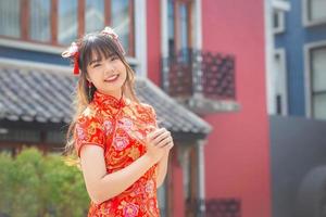Cute Asian young woman in red cheongsam dress in Chinese new year theme stands smiling happily looking at the camera mong old city center in Chinese new year theme. photo