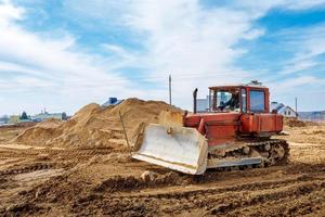 An old orange bulldozer performs work to level the sandy soil photo