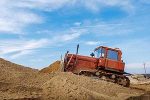 An old orange bulldozer performs work to level the sandy soil photo