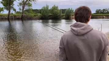 pescatore con un' pesca asta su il fiume banca. uomo pescatore catture un' pesce video