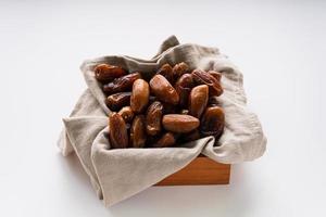 Dried dates fruit in wooden tray with soft napkin isolated on white background. photo
