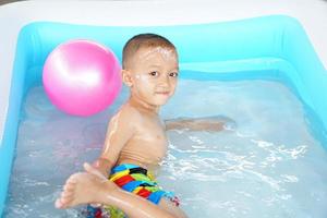 Hot weather. Boy playing with water happily in the tub. photo