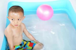 Hot weather. Boy playing with water happily in the tub. photo