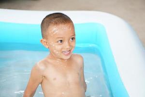 Hot weather. Boy playing with water happily in the tub. photo