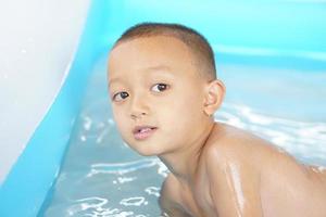 Hot weather. Boy playing with water happily in the tub. photo