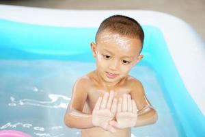 Hot weather. Boy playing with water happily in the tub. photo