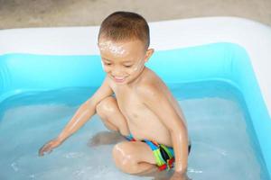 Hot weather. Boy playing with water happily in the tub. photo