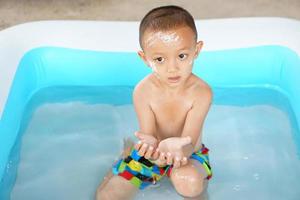 Hot weather. Boy playing with water happily in the tub. photo