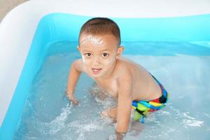 Hot weather. Boy playing with water happily in the tub. photo