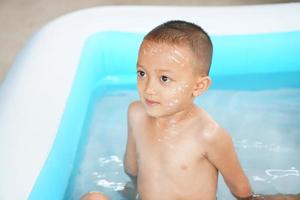 caliente clima. chico jugando con agua felizmente en el tina. foto