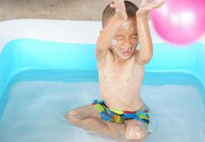 Hot weather. Boy playing with water happily in the tub. photo