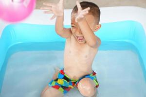 Hot weather. Boy playing with water happily in the tub. photo