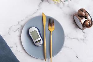 plato con glucosa metro y cuchillería en plato y alarma reloj. diabetes dieta concepto foto