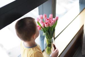 Boy smelling flowers on the window photo