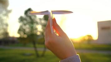 Woman launches paper airplane against sunset background. Concept of wanting to go on vacation or travel video