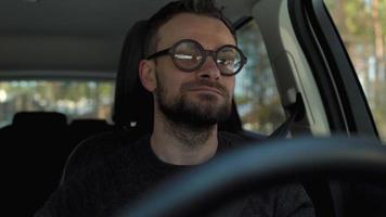 Satisfied bearded man driving a car down the street in sunny weather video