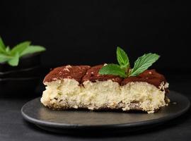 A piece of tiramisu sprinkled with cocoa, on top of a sprig of fresh mint on a black background photo