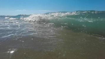 lento movimento do ampla onda quebra em a de praia com espuma e surfar video