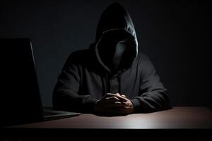 Hacker wearing black hoodie using laptop computer while working on dark background. photo