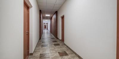 panorama in empty long corridor with red brick walls and doors in interior of modern office photo