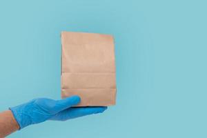 Close up hand in medical glove and holding food paper bag on white background  Isolated background. Concept of Ordering food online and delivery service. photo