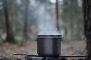 A camping kettle hangs over a fire in the forest in summer. Active holidays on vacation. . photo