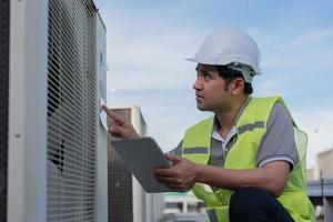 Asian maintenance engineer works on the roof of factory. contractor inspect compressor system and plans installation of air condition systems in construction. technology, online checking photo