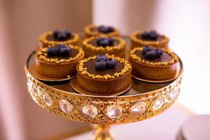 National Dessert Day, October 14. Tasty festive chocolate tartlets decorated fresh blueberies and nuts on gold stand with crystals for party, birthday, valentines day, wedding. French Bakery catering photo