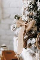 Beautiful Christmas tree decorated with synthetic snow and burlap bow in living room with white brick wall. Merry Christmas, New Year and Happy Holidays background. Eco festive style photo