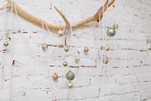 Christmas, New Year composition. Antler with shiny white, gold, green balls and pearl necklaces on white brick wall. Scandinavian cozy home decor. Happy Holidays, Template. Greeting card. 2023 photo