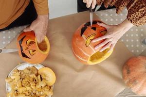 Young couple man and woman on kitchen at home making jack-o'-lantern preparing for halloween, cutting pumpkin. Cutting out faces from a fresh pumpkin. Preparing for the Halloween party celebration. photo