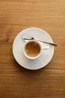 Top view of white porcelain cup with plate and metal spoon of hot coffee with milk on wooden table background. photo