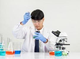 asiático hombre estudiante científico en reactivo mezcla laboratorio en un Ciencias investigación laboratorio con prueba tubos de varios tamaños en el piso en laboratorio química laboratorio blanco antecedentes. foto