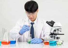 asiático hombre estudiante científico en reactivo mezcla laboratorio en un Ciencias investigación laboratorio con prueba tubos de varios tamaños en el piso en laboratorio química laboratorio blanco antecedentes. foto